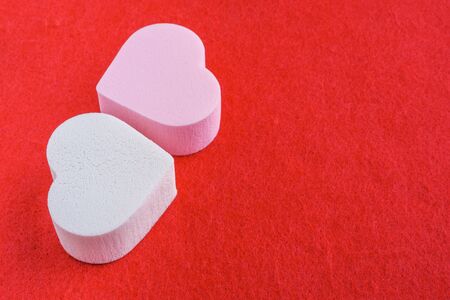 pink and white pastel cosmetic sponges in heart shape on red felt background. skin care and beauty concept. closeup viewの写真素材