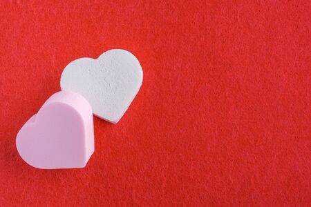 pink and white pastel cosmetic sponges in heart shape on red felt background. skin care and beauty concept. closeup viewの写真素材