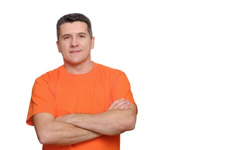 Portrait smiling handsome man wearing orange informal t-shirt with folded arms isolated over white backgroundの写真素材