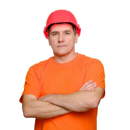 Portrait serious handsome worker with folded arms, wearing construction helmet and orange informal t-shirt isolated over white backgroundの写真素材