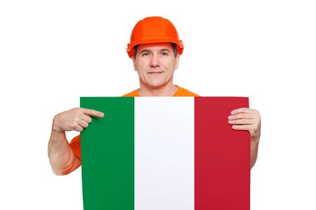 smiling middle-aged worker wearing orange hard hat, holding sheet with italian flag in hands, showing finger to copy space for text. Invitation to work in Italy concept, isolated on white backgroundの写真素材