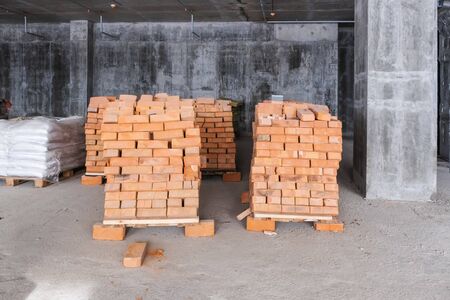pallets with red clay brick and bags of cement at a construction site inside a house under constructionの写真素材