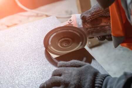 tiler cuts a square hole in the tile using an angle grinder. Finishing works on construction siteの写真素材