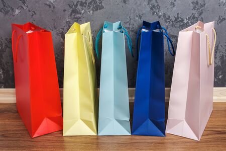 five multicolored paper shopping bags on the wooden floor against a concrete wall background.の写真素材