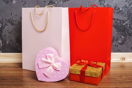 red and pink paper shopping bags and two gift boxes on the wooden floor against a concrete wall background.の写真素材