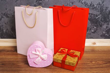 red and pink paper shopping bags and two gift boxes on the wooden floor against a concrete wall background.の写真素材