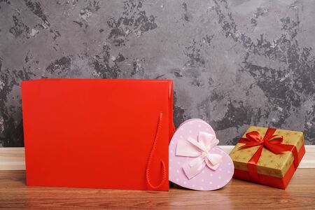 red paper bag and two gift boxes lying on wooden floor against concrete wall background. Copy space for textの写真素材