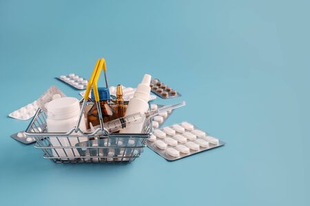 Shopping basket with medicinal pills and tablets. Variety of pills, drugs, spay, syringe in mini basket on blue background. Pharmacy Shopping Concept, copy spaceの写真素材