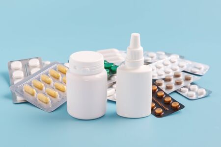 Two white bottles foreground and pile of various shapes and sizes of drugs in different packaging on a blue background.の写真素材