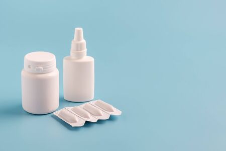 two white plastic bottles for pills without labels and suppositories packaging on blue background. Copy space for textの写真素材