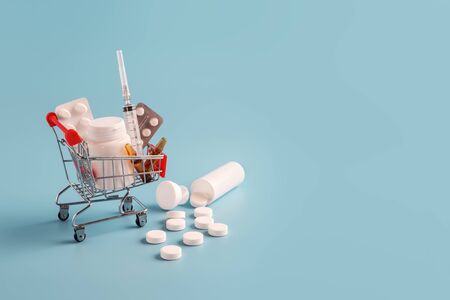 Shopping cart with medicinal pills and scattered tablets. variety of pills, drugs, spay, syringe in mini basket on blue background. Pharmacy Shopping Concept, copy spaceの写真素材