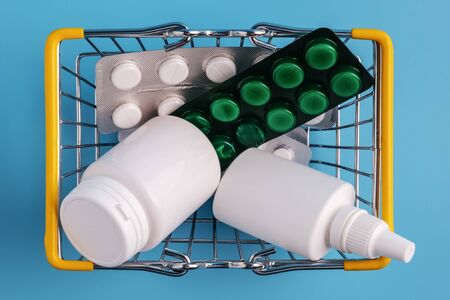 Shopping basket with medicinal pills and tablets closeup. Variety of drugs, bottles, spray in mini basket on blue background. Pharmacy Shopping Concept. top viewの写真素材