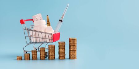 stacks of coins in a row ascending, shopping trolley cart filled medicinal tabletsand pills on background, selective focus. most expensive drugs or rising drug prices concept, copy space for textの写真素材