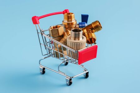 red shopping cart with plumbing fittings closeup. Brass ball valve, y filter, tee and polypropylene coupling in mini basket on blue background. shopping concept.の写真素材