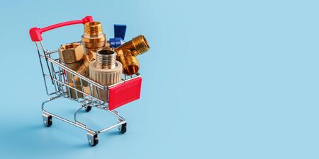 red shopping cart with plumbing fittings closeup. Brass ball valve, y filter, tee and polypropylene coupling in mini basket on blue background. shopping concept, copy spaceの写真素材