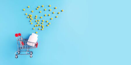 Shopping cart fell down with yellow medical drugs scattered on blue background. Copy space for advertising drugstore, online pharmacy and pharmaceutical company business, flat layの写真素材