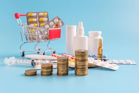 stacks of coins in a row ascending, shopping trolley cart filled medicinal tablets and pills and pile drugs on background, selective focus. most expensive drugs or rising drug prices concept.の写真素材