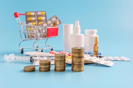 stacks of coins in a row ascending, shopping trolley cart filled medicinal tablets and pills and pile drugs on background, selective focus. most expensive drugs or rising drug prices concept.の素材 [FY310141026790]