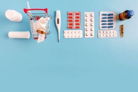 Shopping cart with medical drugs and thermometer, bottles, blisters pills and syringe on blue background. Copy space for advertising drugstore, online pharmacy or pharmaceutical company, flat layの写真素材