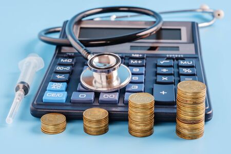 stacks of coins in a row ascending. Calculator, syringe and sthetoscope on blue background, selective focus. cost of health care conceptの写真素材