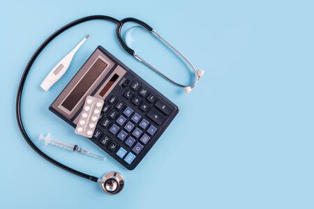 Calculator, syringe, thermometer, pills and sthetoscope on blue background. cost of health care conceptの写真素材