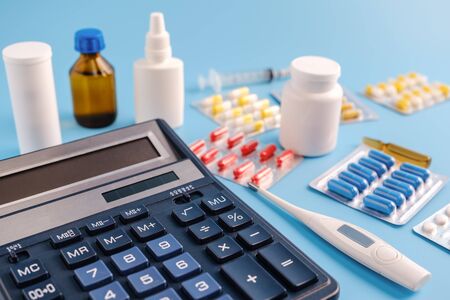 Calculator, thermometer and pile of drugs on blue background. cost of health care conceptの写真素材