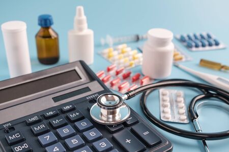Calculator, sthetoscope and pile drugs on blue background. cost of health care conceptの写真素材