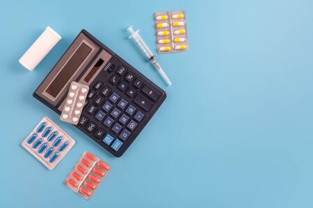 Calculator, syringe, pills and medicine bottle on blue background. cost of health care concept, copy space, flatlayの写真素材