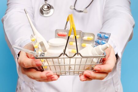Doctor's hands are holding shopping cart with various pills, tablets, syringe, thermometer and medicine bottles closeupの写真素材