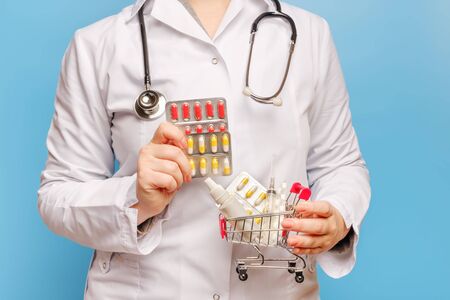 one doctor hand holds out pills close-up, and the other holds a shopping trolley with pills, syringe and bottle of medicineの写真素材