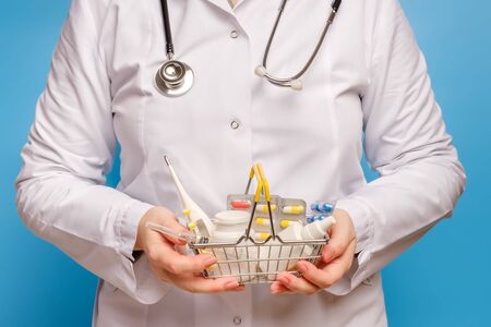 Doctor's hands are holding shopping cart with various pills, tablets, syringe, thermometer and medicine bottles closeupの写真素材