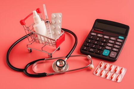 shopping trolley cart filled tablets, medicine bottle, syringe and calculator on pink background, selective focus. most expensive drugs or rising drug prices concept, copy spaceの写真素材