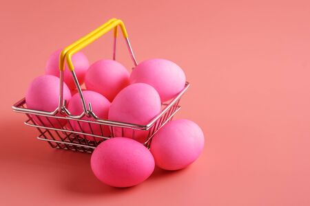 Easter eggs on pink background and shopping cart with eggs. Easter shopping and sale, copy space,の写真素材