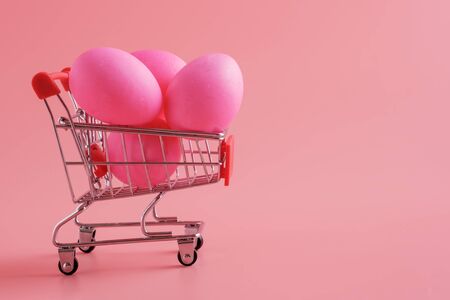 Trolley Shopping cart with Easter eggs on pink background. Festive Easter shopping and sale, copy spaceの写真素材