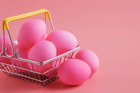 Easter eggs on pink background and shopping cart with eggs closeup. Easter shopping and sale, copy space,の写真素材