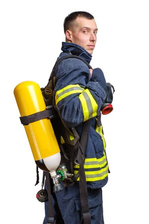 Young caucasian firefighter posing in profile with Full Facepiece Respirator and Breathing Air Cylinder Assembly on his back in fireproof uniform isolated on white backgroundの写真素材
