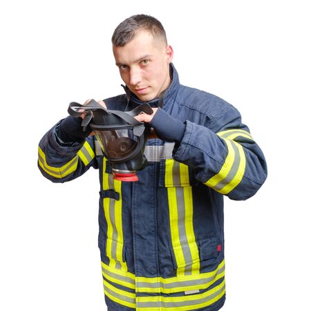 young caucasian fireman in uniform puts full facepiece respirator over his head. Isolated on white background.の写真素材