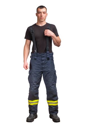 Young firefighter wears black t-shirt standing and pull suspender on his fireproof pants isolated on white background.の写真素材