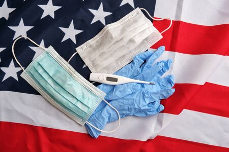 Used surgical protective masks, gloves, digital thermometer on american flag background. Covid-19 quarantine. Flat lay, top viewの写真素材