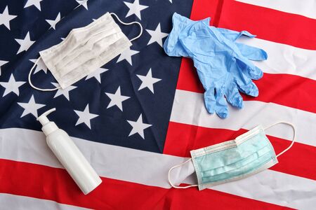 Frame from used protective masks, gloves and sanitizer pump bottle on american flag background. Covid-19 quarantine. Flat lay, top view, copy spaceの写真素材