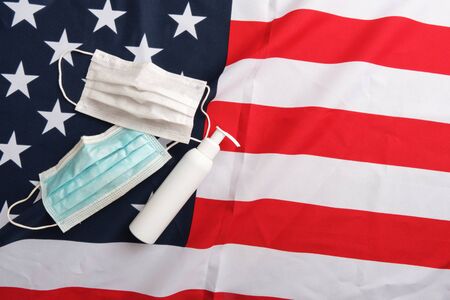 Used protective masks and sanitizer pump bottle on american flag background. Covid-19 quarantine. Flat lay, top view, copy spaceの写真素材