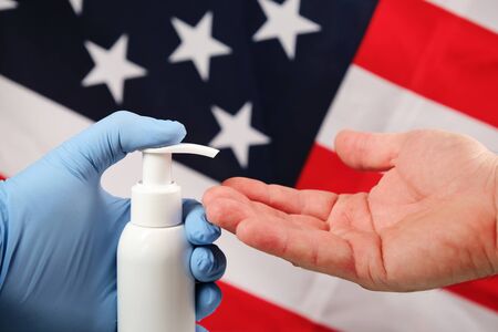 Doctors hand in blue medical glove applying antiseptic alcohol gel on hand without a glove to prevent infections coronaviruses, bacteria and germs, on american flag backgroundの写真素材
