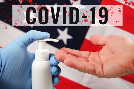 Doctors hand in blue medical glove applying antiseptic alcohol gel on hand without a glove to prevent infections on american flag background. inscription covid-19 and blood dropsの写真素材