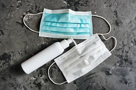 Two used protective masks and sanitizer bottle closeup on gray concrete background. Covid-19 quarantine. Flat lay, top viewの写真素材