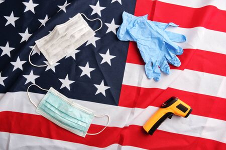 Frame from used protective masks, gloves and non-contact infrared thermometer on american flag background. Covid-19 quarantine. Flat lay, top view, copy spaceの写真素材