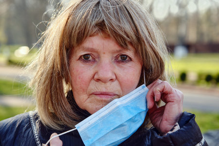 portrait of elderly woman putting medical mask on her face outdoors. Closeup view