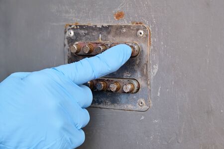 finger in blue latex gloves presses a button on the panel of the mechanical combination lock on the iron front door, metal door.の写真素材