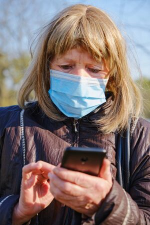 Caucasian elderly woman wears mask for protect coronavirus outbreak and use smartphone to talk with her family and friends. Vertical orientationの写真素材