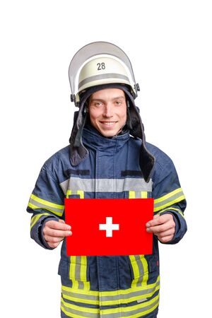 young smiling firefighter wearing uniform and helmet looking to the camera and holding paper sheet with swiss flag in hands. isolated on white backgroundの写真素材