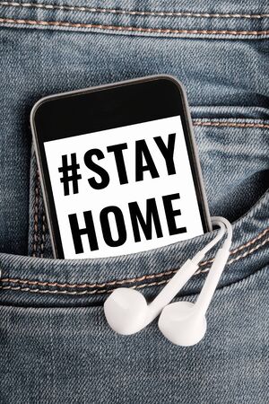 modern smartphone and earphones on denim textile. text on phone screen encourages stay at home to prevent virus infection. Vertical orientationの写真素材